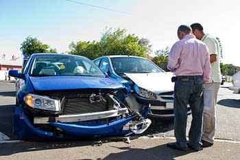 Two men looking at car accident and filing insurance claims